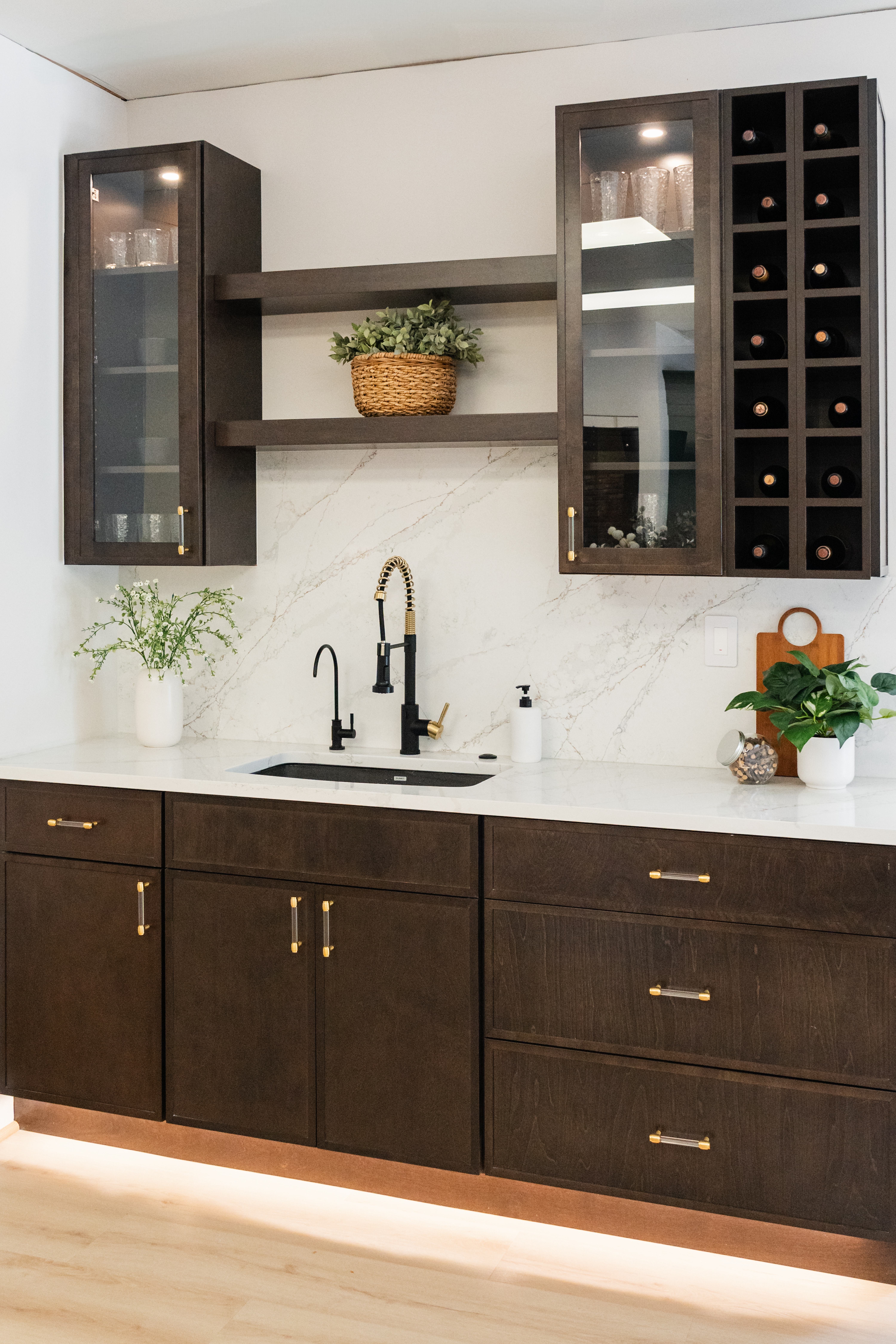 Modern kitchen with dark wood cabinets, a white marble backsplash, glass-fronted upper cabinets, a wine rack, potted plants, open shelves, and under-cabinet lighting—perfect inspiration for your next kitchen remodeler or remodeling project.